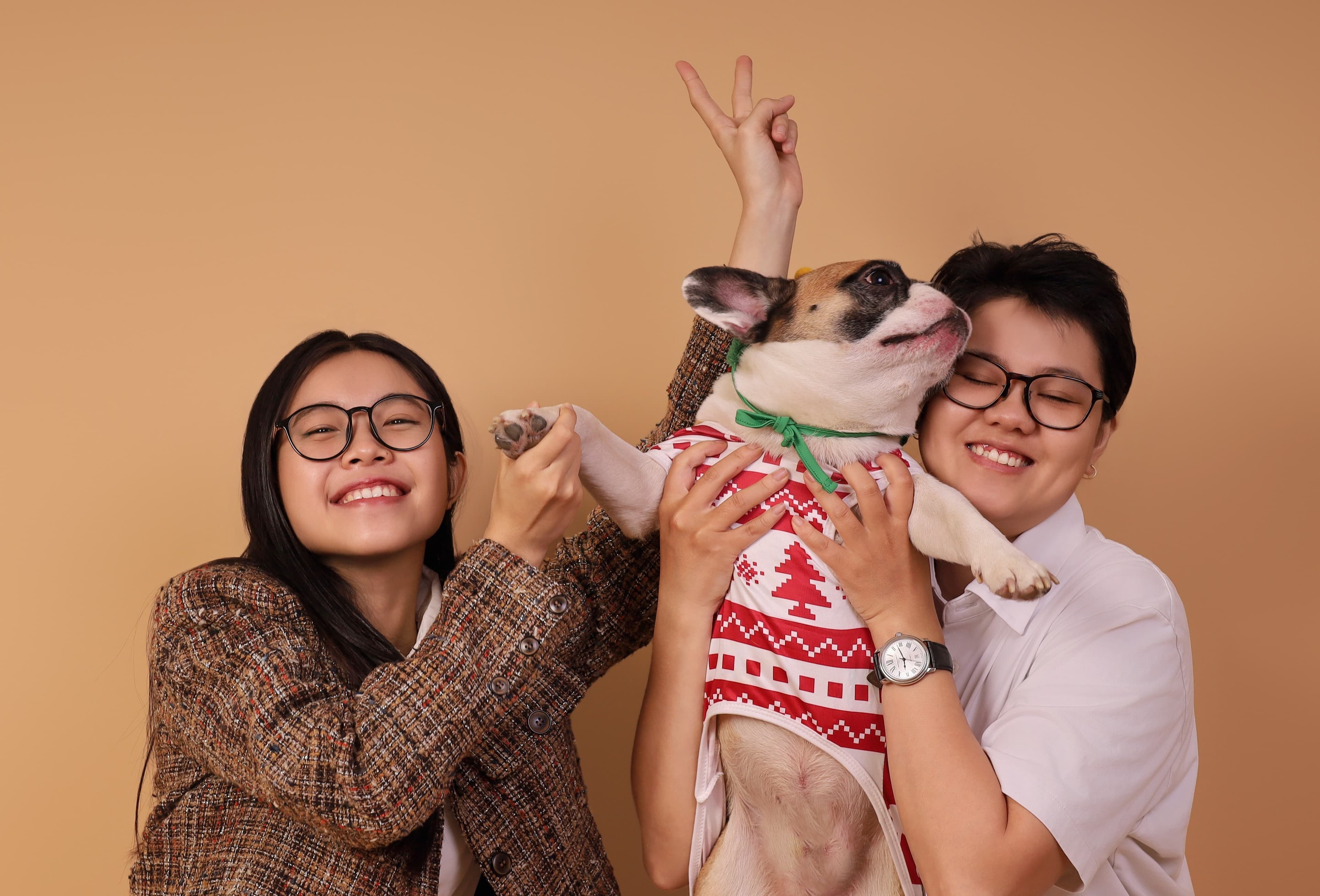 Two people taking a photo with a dog dressed in a Christmas sweater at Petcial Studio.